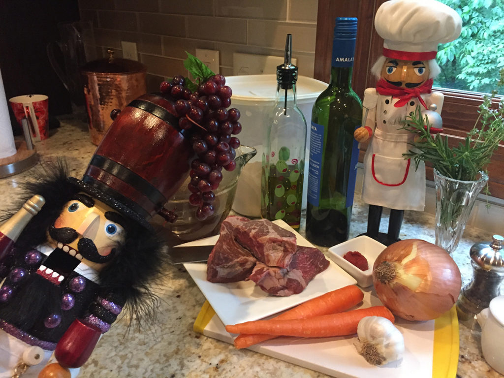 Short ribs, carrots, onion, garlic tomato paste on a cutting board With a nutcracker that looks like a chef and another nutcracker that looks like a sommelier