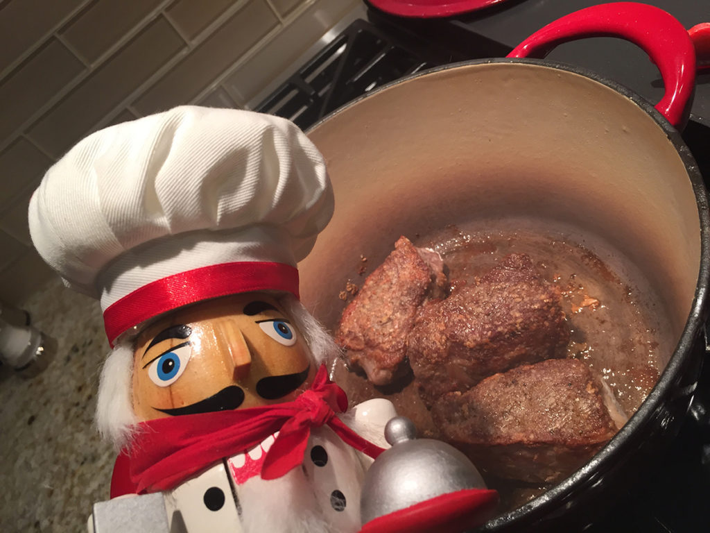 3 browned beef short ribs in a dutch oven with a nutcracker that looks like a chef.