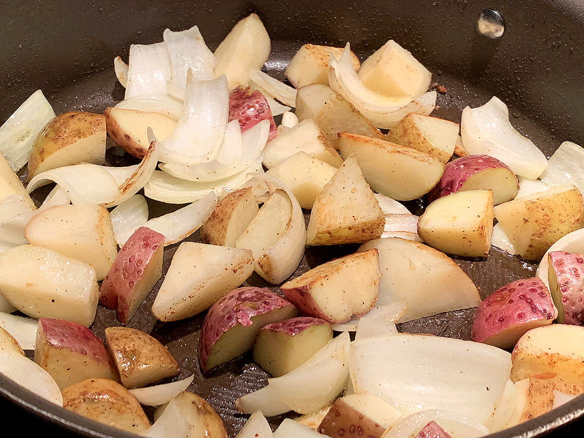 Large chunks of potatoes and onions in a skillet. 