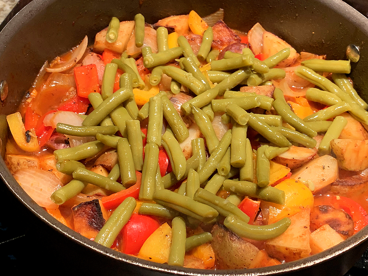 Skillet filled with, onions, red and yellow bell peppers and green beans.
