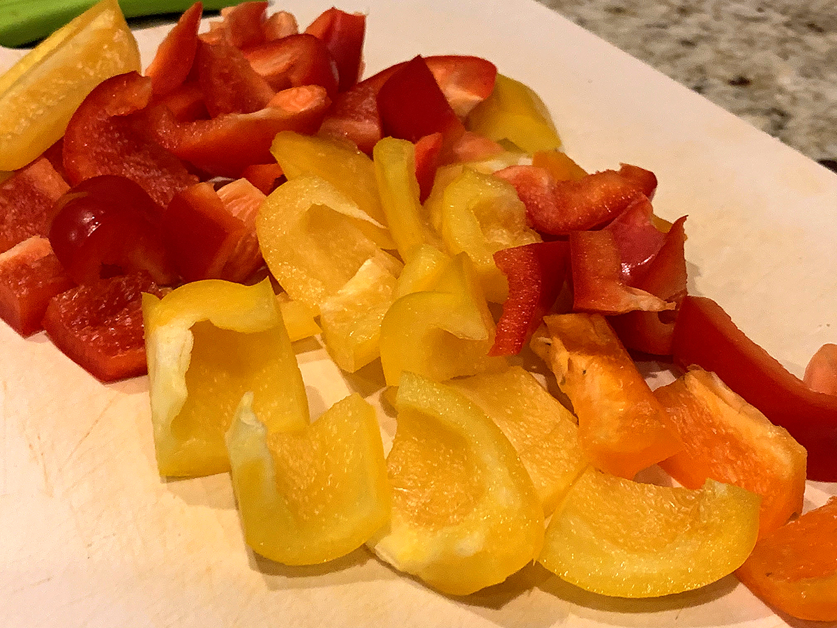Red and yellow bell peppers cut into large chunks on a white cutting board. 