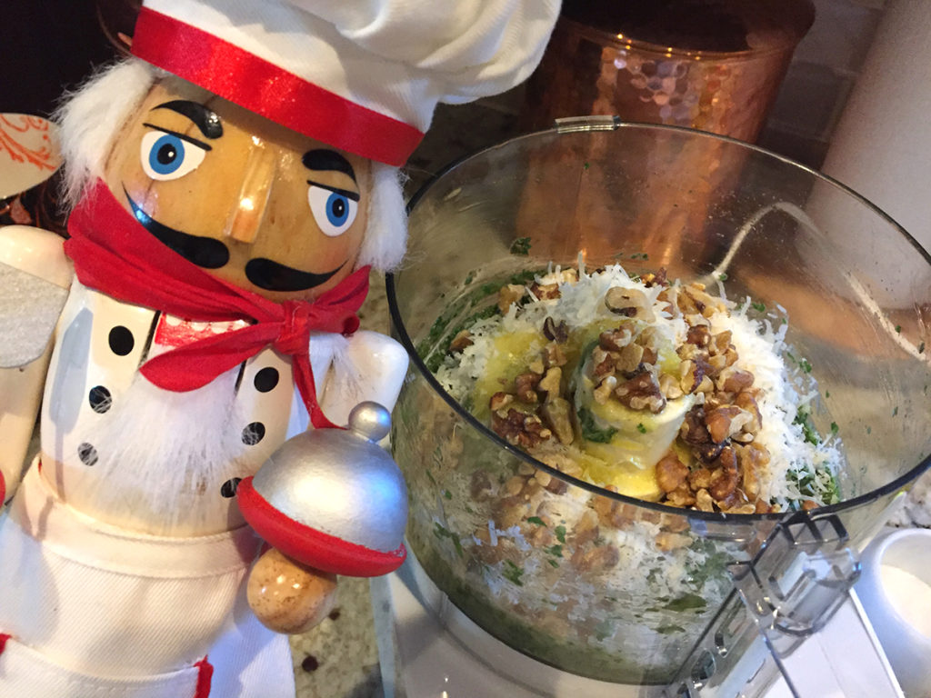 Walnuts and cheese added to the food processor to make basil pesto. There's a nutcracker in the foreground who looks like a chef