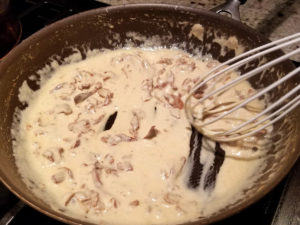Chanterelle cream sauce in a non-stick skillet with a white rubber whisk.