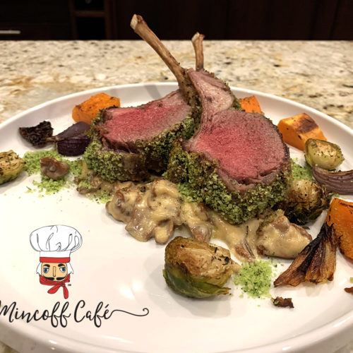 Two medium rare herb crusted racks of lamb with a chanterelle cream sauce on a round white plate with roasted butternut squash, brussels sprouts and red onions.