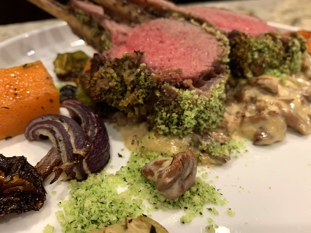Close up image of medium rare herb crusted rack of lamb with roasted veggies and a chanterelle cream sauce. 