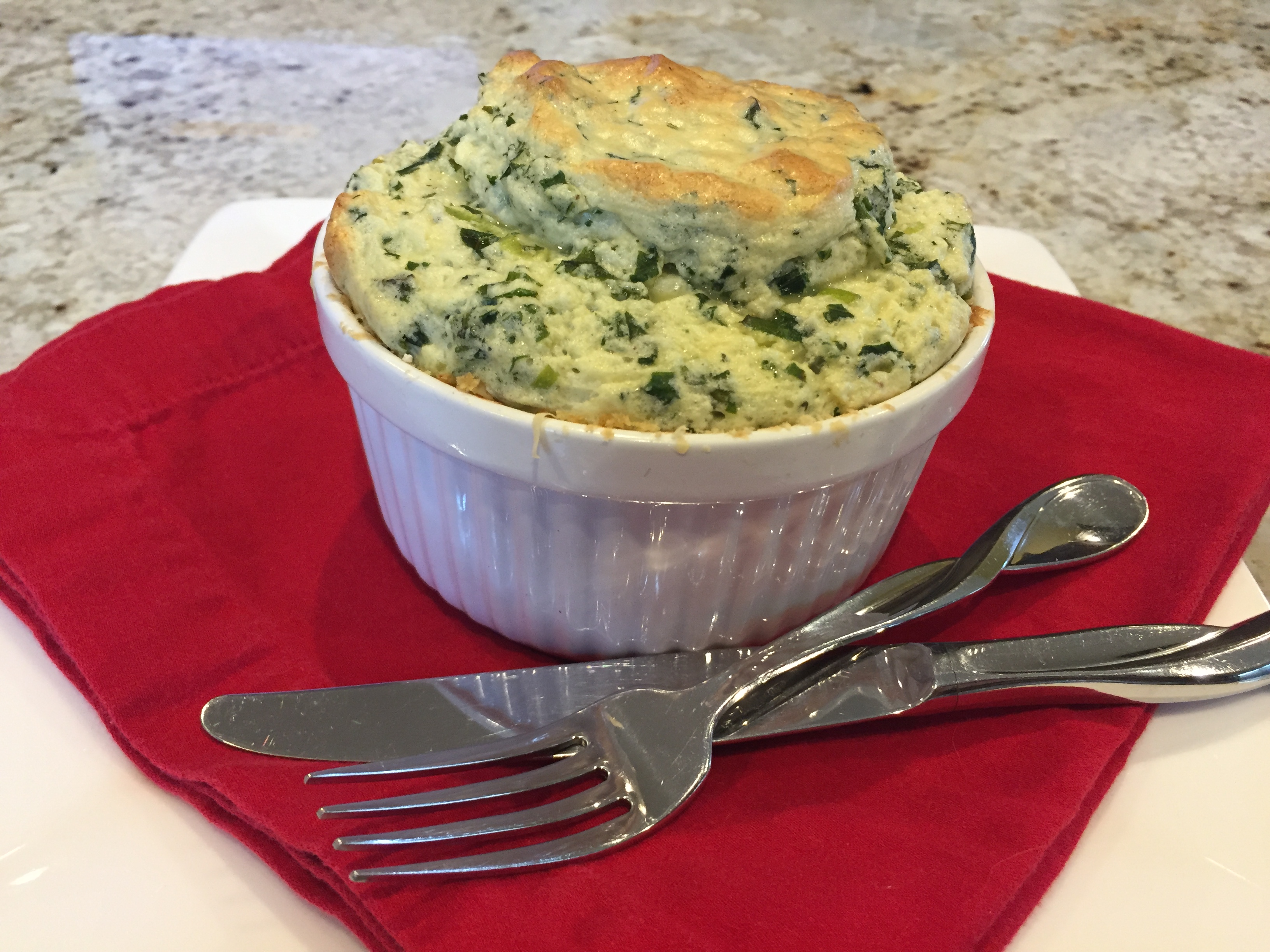 Small kale & cheddar souffle in a white ramekin on a red napkin.