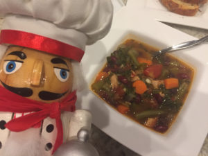 Minestrone Soup in a square white bowl with a nutcracker who looks like a chef in the foreground on the left.