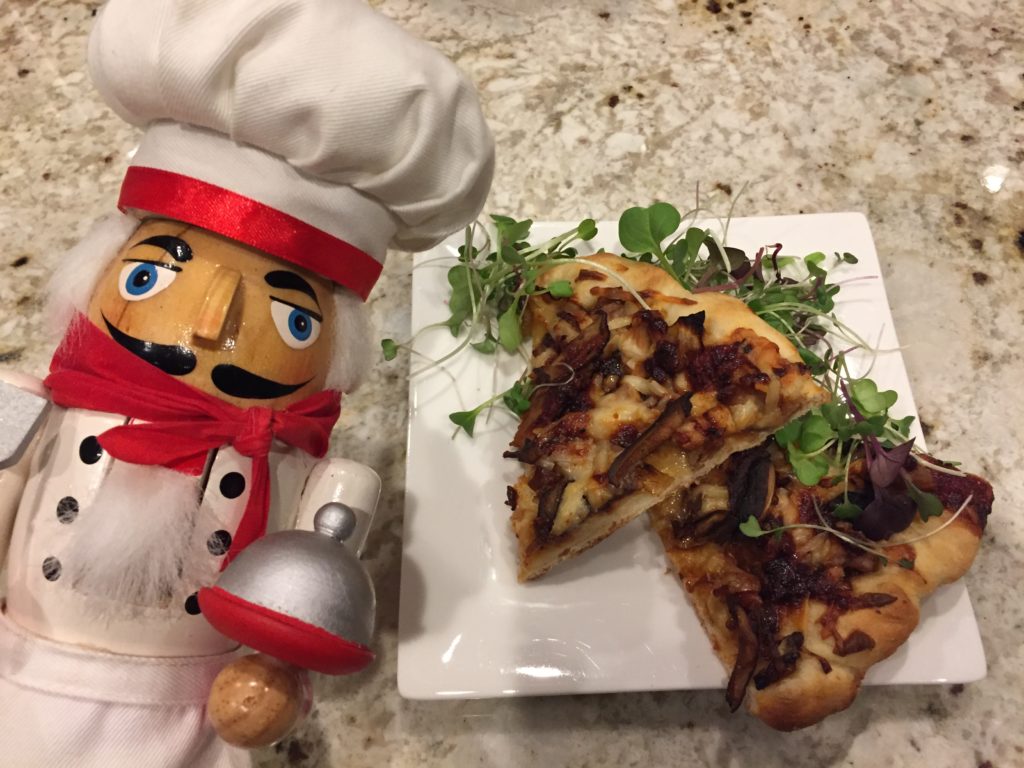 Two triangle slices of duck pizza on a square white plate. There's a nutcracker in the foreground that looks like a chef.
