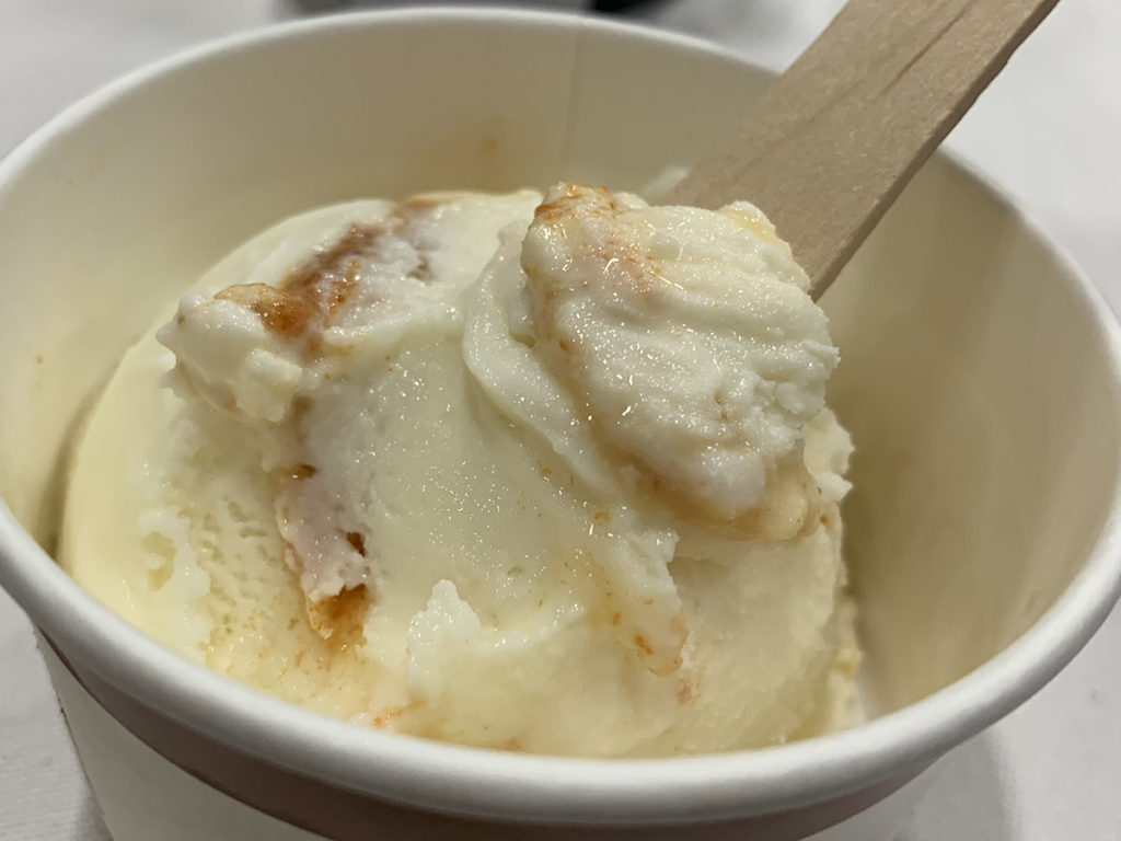 single scoop of white and caramel swirled ice cream in white paper bowl with wooden spoon