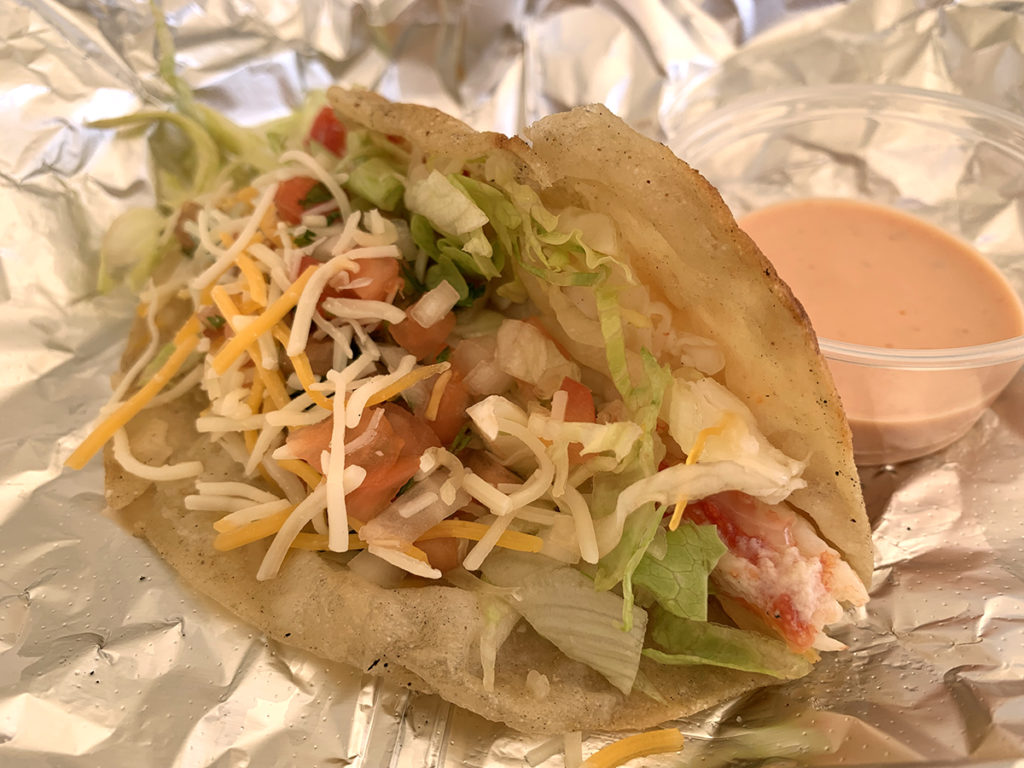 King crab taco with lettuce, cheese and pico de gallo on a four tortilla with cup of sauce, all on foil