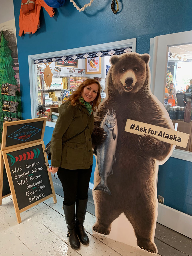 Stacey Mincoff standing next to a large bear cutout with a sign that says #askforAlsaka