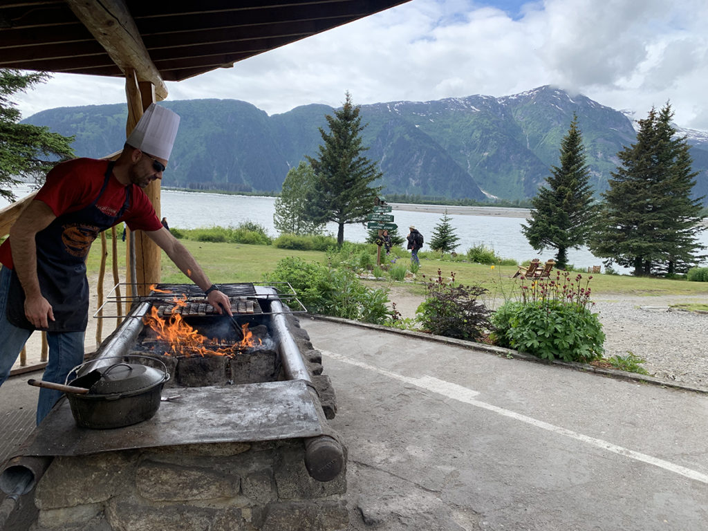 chef cooking on outdoor grill with mountains in the background
