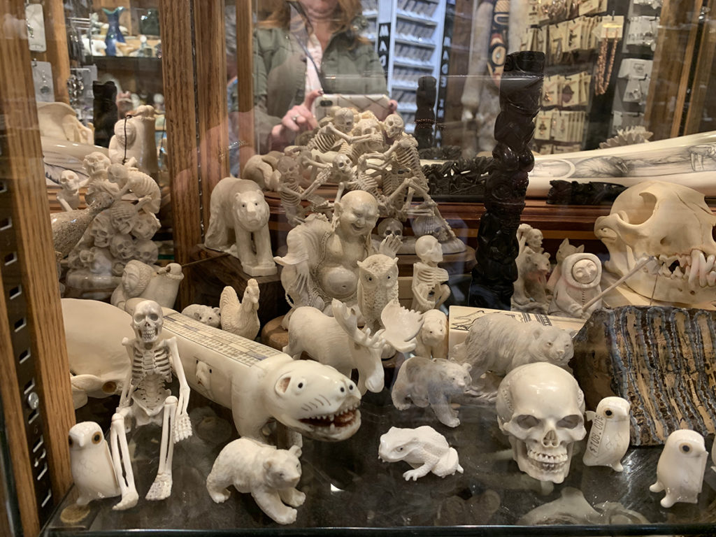 Multiple native bone carvings of skeletons, bears, owls, moose, frog and totem pole in glass case.