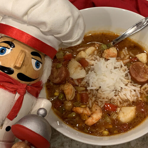seafood & chicken gumbo in a white bowl on a tan granite countertop with a nutcracker that looks like a chef