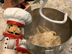Homemade English muffin dough on beater of a stand copper colored stand mixer with a nutcracker that looks like a chef to the left.