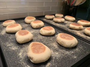 Homemade English muffins cooking on a pair of griddles.