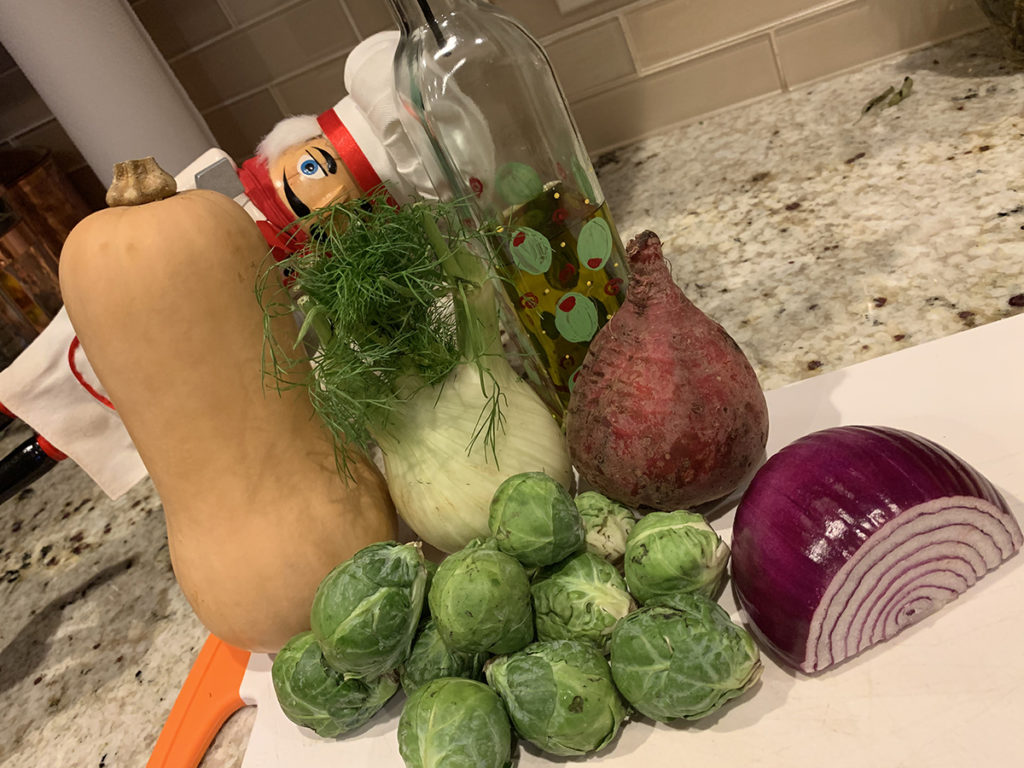 Pepe the nutcracker who looks like a chef hiding behind fall veggies that are going to be roasted. Butternut squash, fennel bulb, red beet, red onion and brussels sprouts