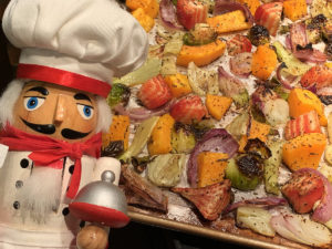 chunks of roasted fall veggies (butternut squash, brussels sprouts, red beets, fennel bulbs and red onions) on a sheet pan with a nutcracker that looks like a chef in the foreground..