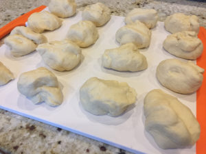 16 small balls of dough on a white cutting board with orange accents on each end.