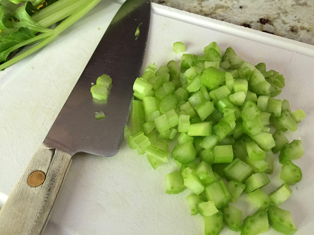 Chopped celery with a chef knife on a white cutting board.
