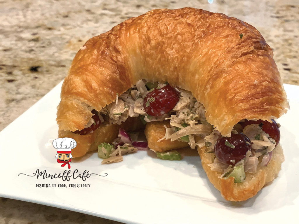 Turkey salad sandwich with turkey, celery, red grapes and onions on a croissant, sitting on a white square plate.