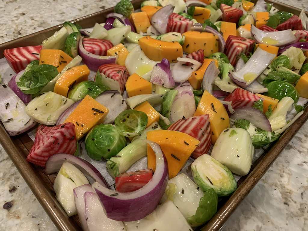 Raw mixed fall veggies ((butternut squash, red onions, brussles sprouts, fennel bulb and candy cane beet root) on a sheet pan ready for the oven.