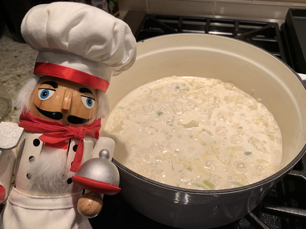 Pepé the nutcracker next to his very pale yellow cauliflower soup in a white dutch oven, still on the stove.