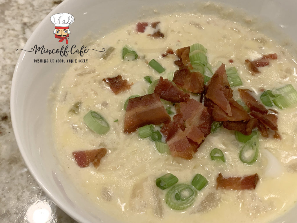 Pale yellow cauliflower soup in a white bowl, garnished with chopped green onions and bacon.