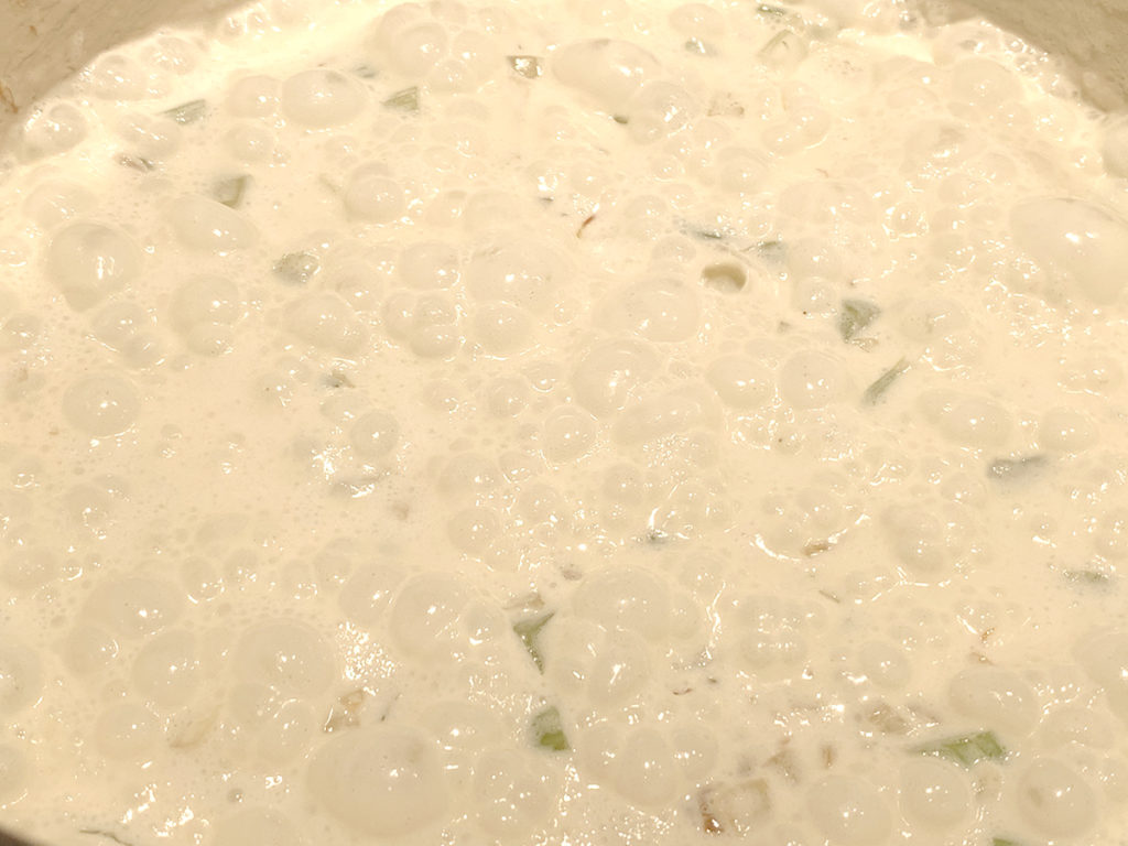 Hot bubbling cream with celery and onions in a white dutch oven.