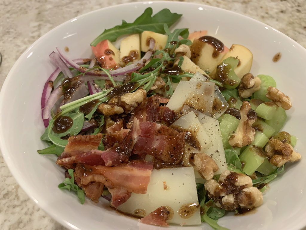 Bacon, Apple, celery, red onions, walnuts, manchego cheese and arugula salad in a while bowl. Topped with a balsamic vinaigrette.