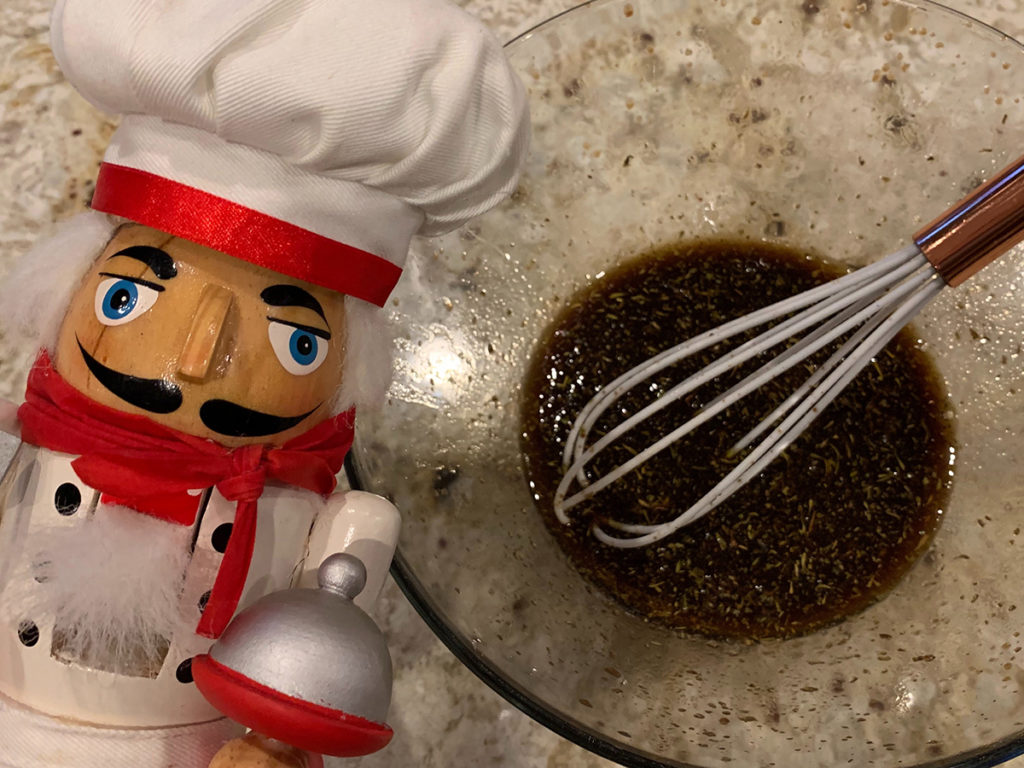 homemade balsamic vinaigrette in a glass bowl with a white silicone whisk that has a copper handle. There's a nutcracker that looks like a chef in the foreground on the left.