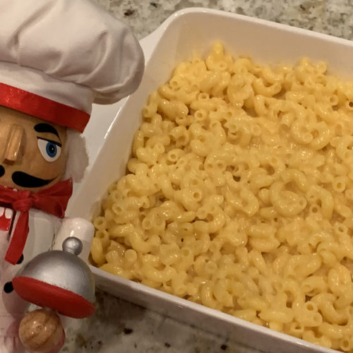Mac and cheese in a square white casserole dish with a nutcracker in foreground that looks like a chef.