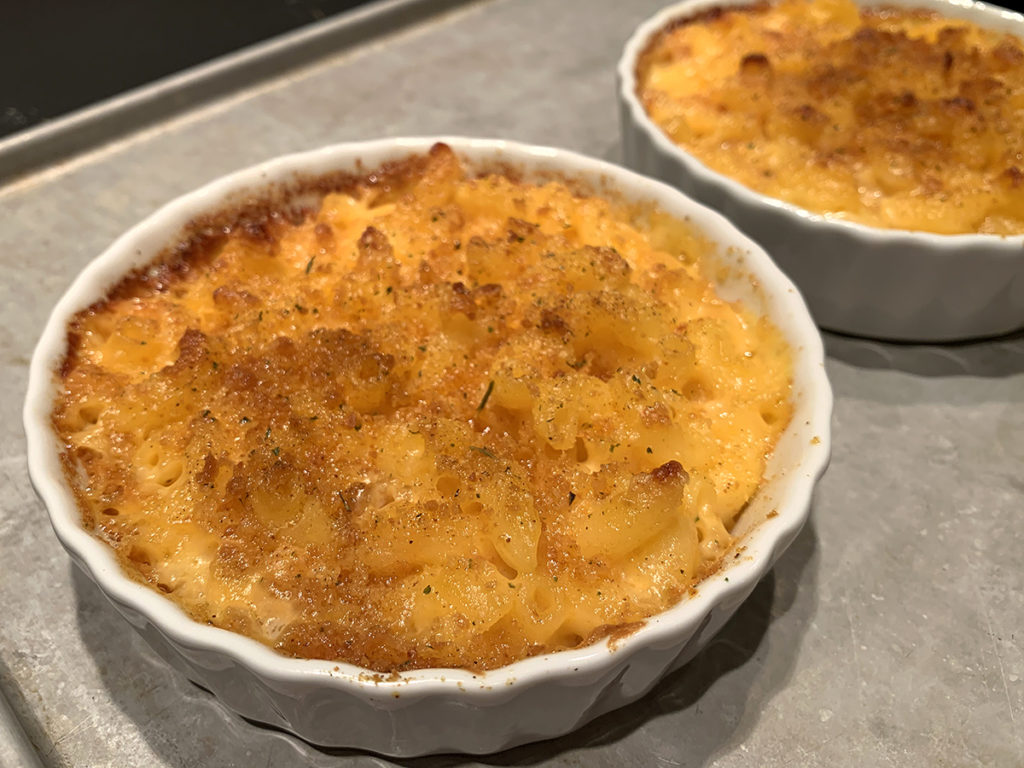 two round white ramekins with baked mac and cheese in them, sitting on a sheet pan.