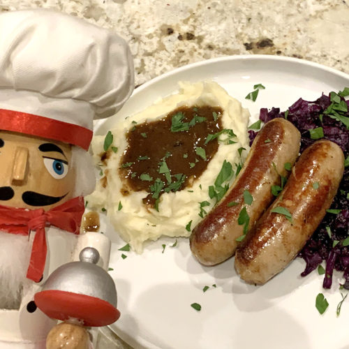 Bangers & Mash with Fried Reg Cabbage, sprinkled with parsley and a nutcracker that looks like a chef in the foreground.