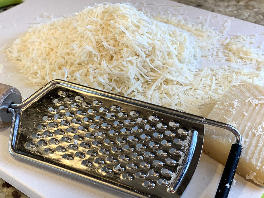 Pile of Parmisiano cheese with a hand grater on a white cutting board