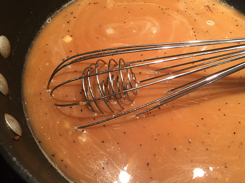 Brown onion gravy in a dark grey sauce pan with a wire whisk
