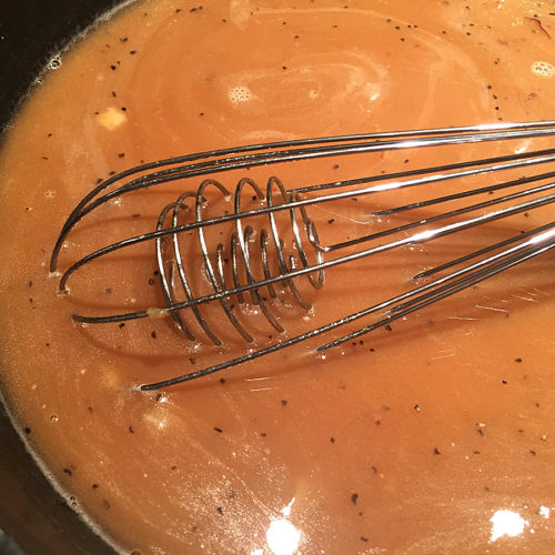 Brown onion gravy in a dark grey sauce pan with a wire whisk