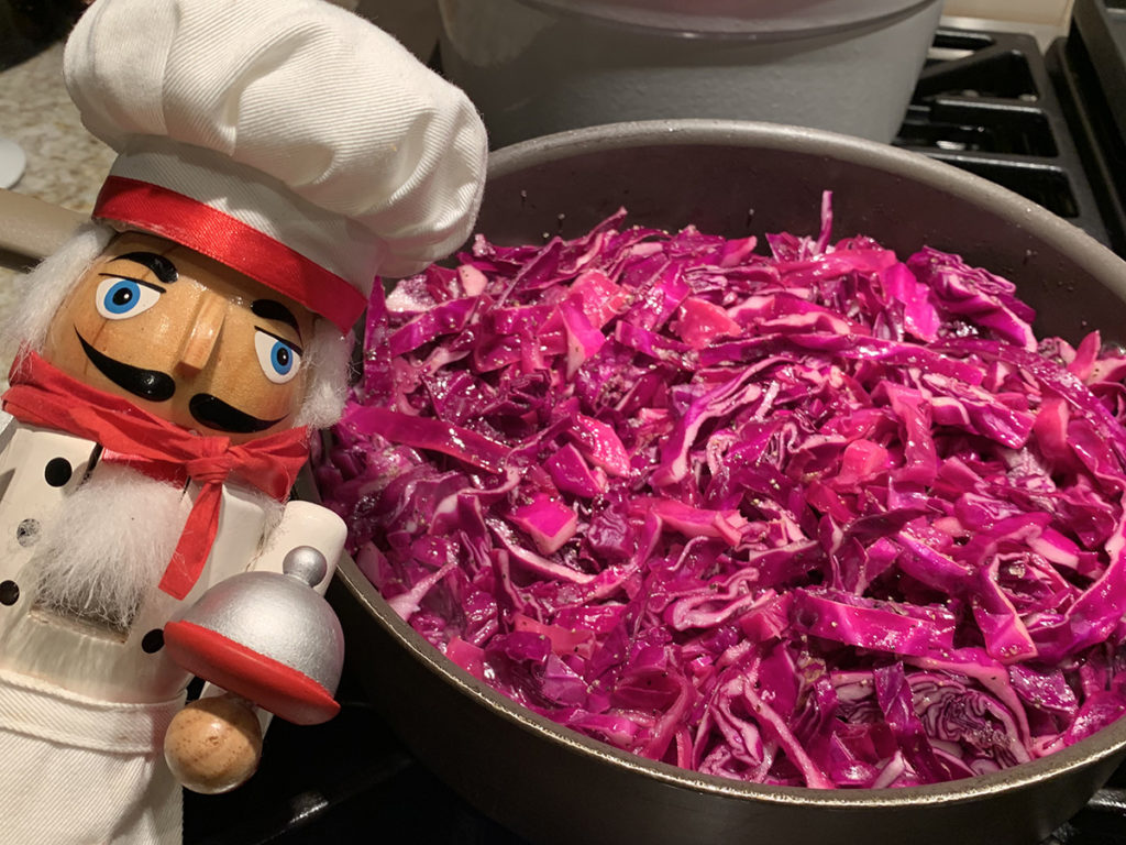 Fried red cabbage in a skillet with a nutcracker that looks like a chef in the foreground.