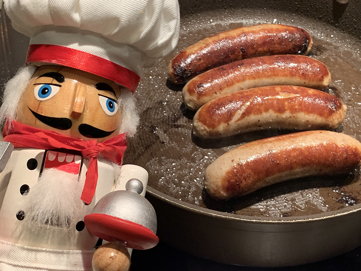 4 pork sausages or bangers in a skillet with a nutcracker that looks like a chef in the foreground.