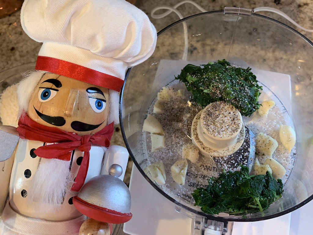 Stinging nettle leaves, garlic cloves, salt and pepper in a food processor. And a nutcracker who looks like a chef in the foreground.