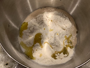 Flour, honey, water, oil and foamy yeast in a stainless steel bowl.