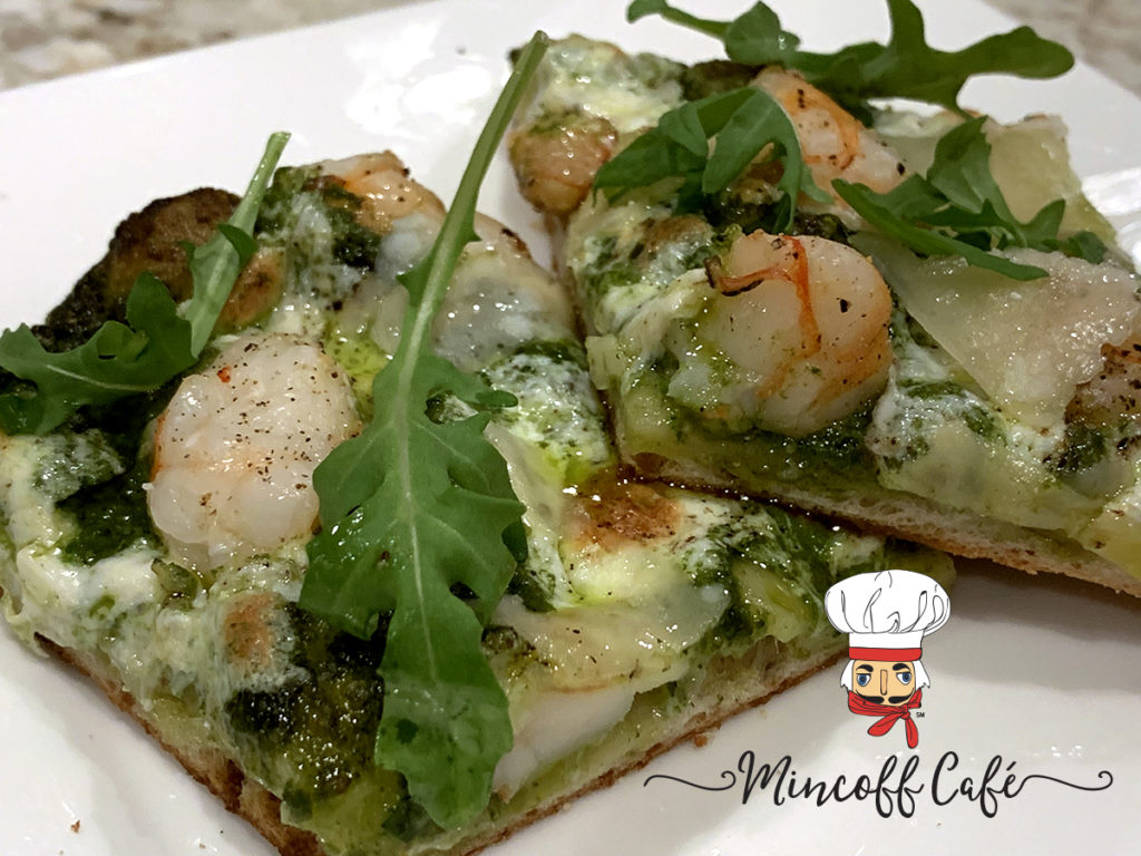 Two square slices of shrimp and nettle pesto pizza with arugala on a white plate with the minoff cafe logo in the bottom right corner.