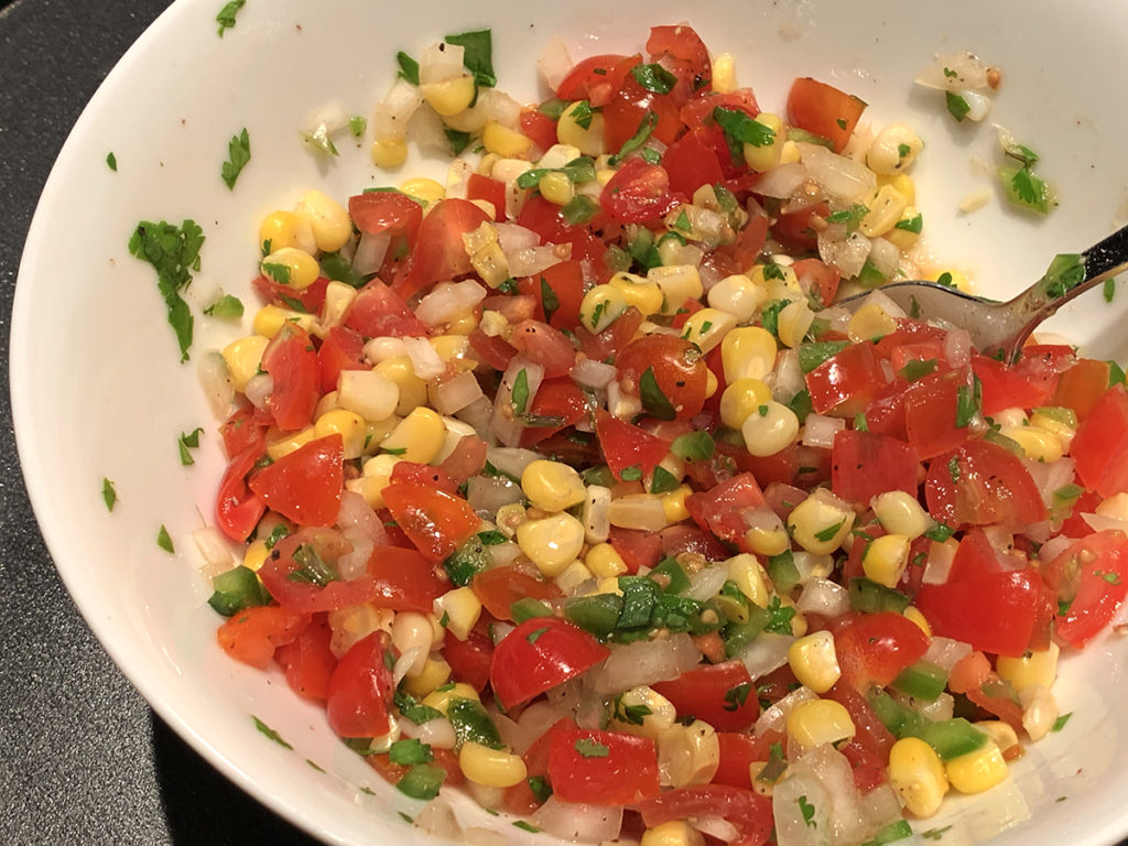 Pico de gallo made of chopped tomatoes, onions, jalepenos, cilantro, yellow corn and lime juice in a round white bowl. 