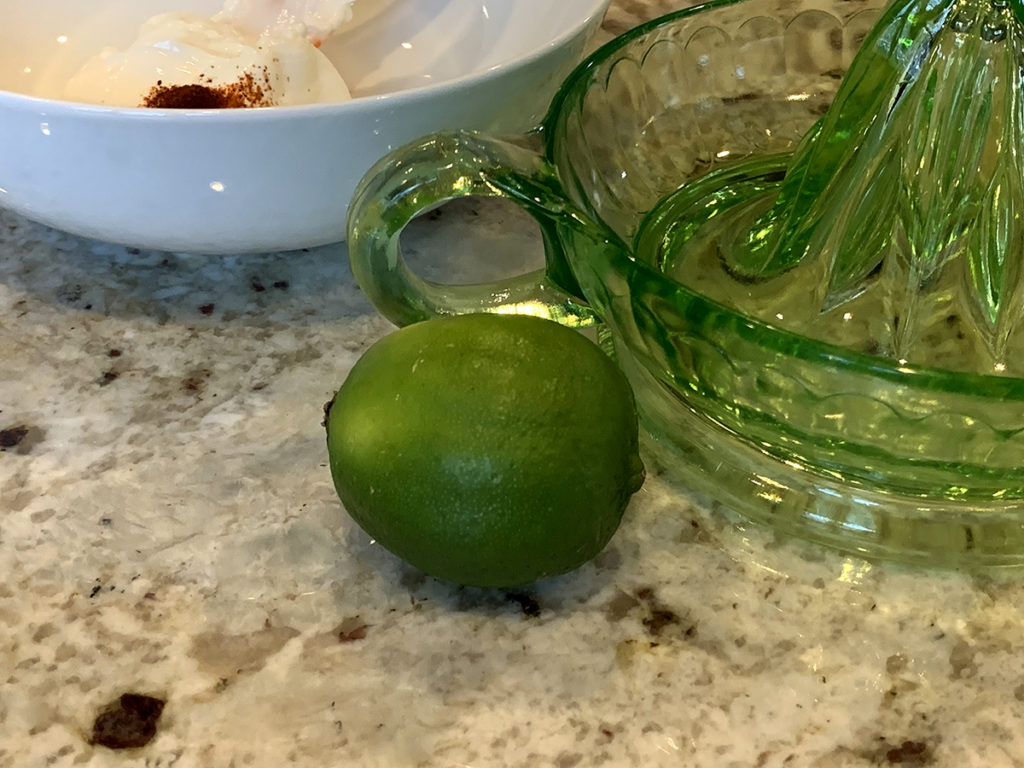 One lime, green glass juicer and a white round bowl sitting on a granite counter. 