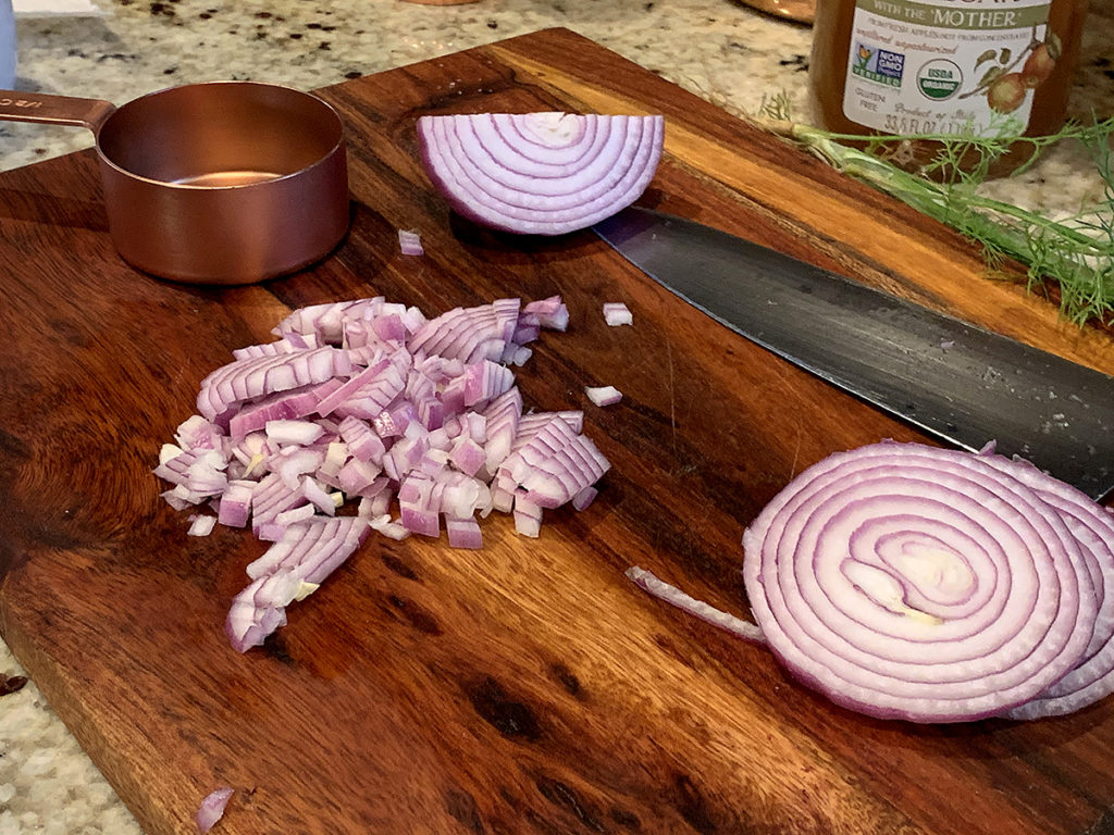 Shopped red onions on a nice wood cutting board with a copper measuring cup and a chef knife. 