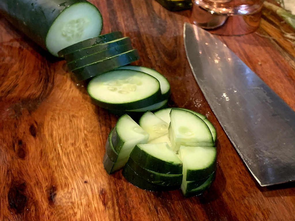 Cutting cucumber into small bite size pieces (sliced, then quartered). All on a nice wood board with a chef knife. 