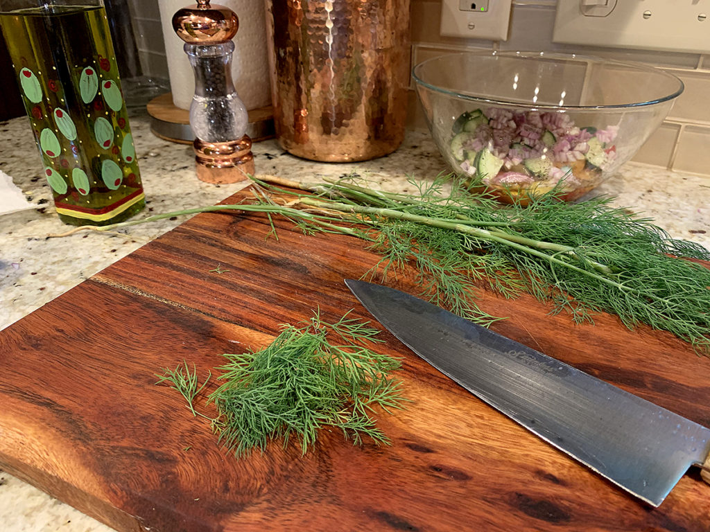 Fresh dill weed sitting on a cutting board waiting to be roughly chopped. 