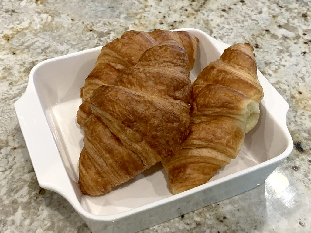 Three large croissants sitting in a square, white dish.