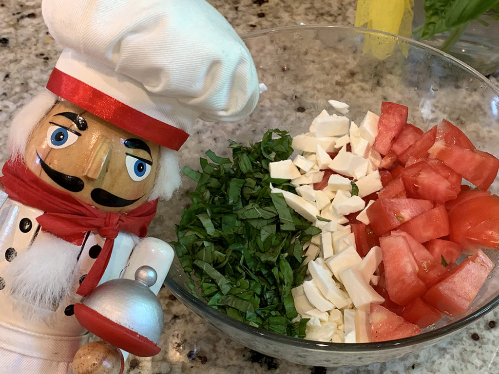 Basil, fresh mozzarella and tomatoes arranged in rows to represent the Italian flag. There's a nutcracker in the foreground who looks like a chef.