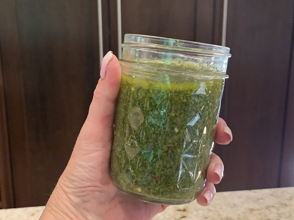 Jar of homemade culantroHand holding a jar of green pesto asian crack sauce.